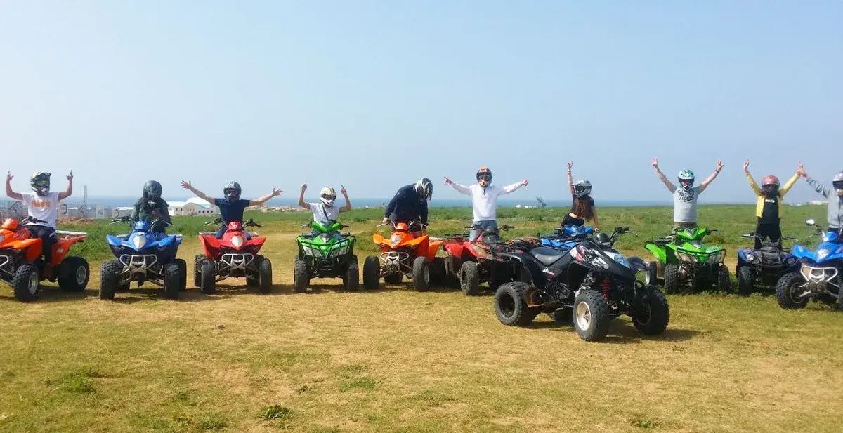 A group posing beside parked quad bikes in an open coastal landscape
