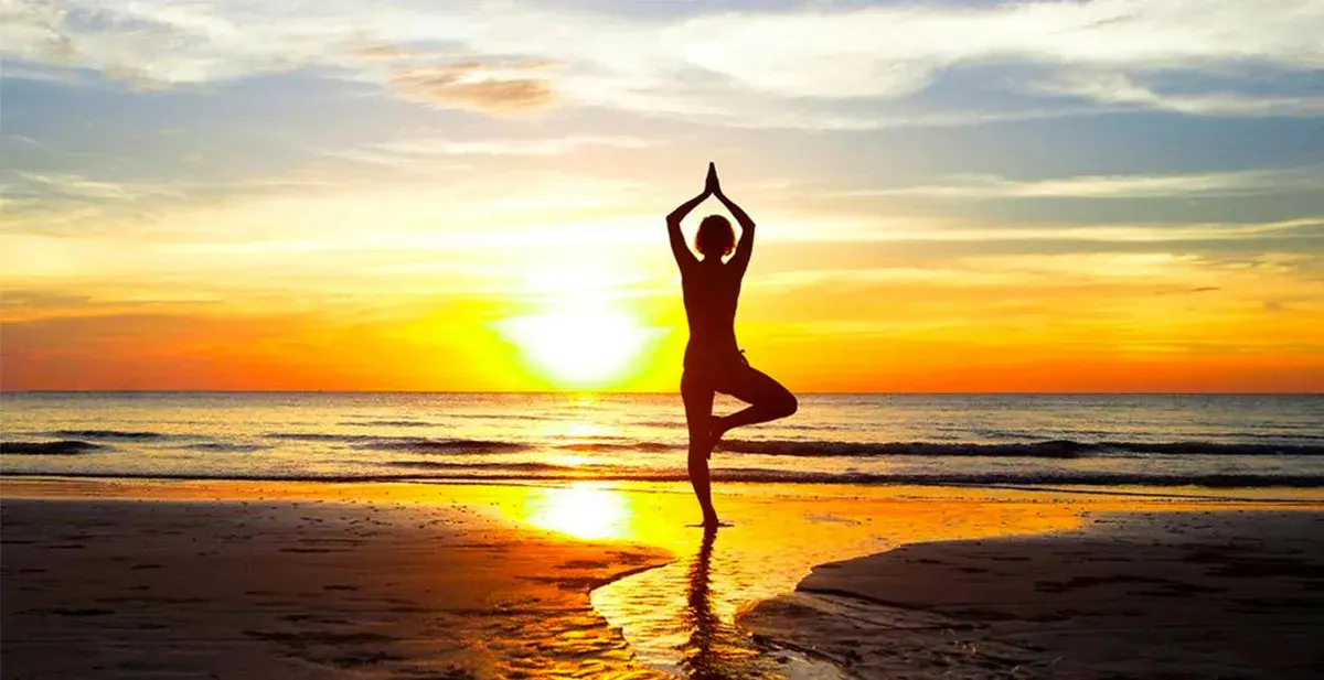 A person holding a standing yoga pose on the beach at sunset