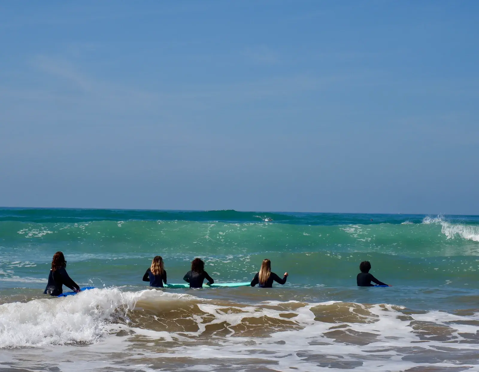 Five surfers with their boards in the ocean, facing an approaching wave